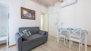 A modern living room with a grey sofa, a small table with chairs, and a painting on the wall. - Apartments La perla - Apartment with Balcony (Carloforte)