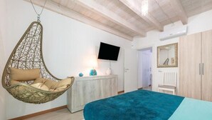 A bedroom with a hanging chair, a bed with a patterned bedspread, a television on the wall, and a wardrobe. - Apartments La perla - Apartment with Balcony (Carloforte)