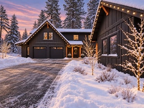 Une cabane en bois sombre, dotée d’un garage, entourée d’un paysage enneigé et d’arbres.
