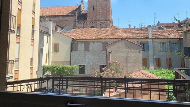 A view from a balcony overlooking a historic building with a tall tower, featuring a courtyard with a fountain and surrounding buildings. - Residence Clementina, 155sqm of charm in the historic center (Padova)