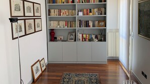 A room with a bookshelf, framed pictures on the wall, a rug, and a table with a glass. - Residence Clementina, 155sqm of charm in the historic center (Padova)