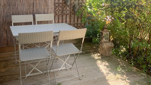 Une terrasse extérieure avec une table et des chaises, entourée d’une clôture en bambou et de verdure.