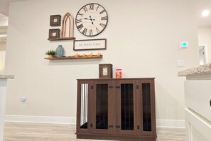A room with a large wall clock, a decorative sign, a wooden cabinet, and a shelf with small items. - Dog-Friendly Beach Home · Golf Cart · Beach Access (Port St Joe)