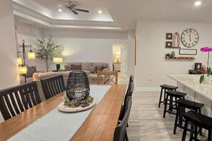 Un coin repas avec une table en bois, des chaises noires, une décoration centrale en fibres tressées et un ventilateur de plafond.