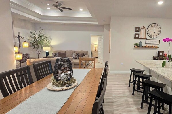 Un coin repas avec une table en bois, des chaises noires, une décoration centrale en fibres tressées et un ventilateur de plafond.