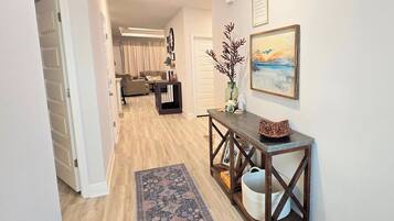 A hallway with a wooden floor, a console table with decorative items, a rug, and a painting on the wall.