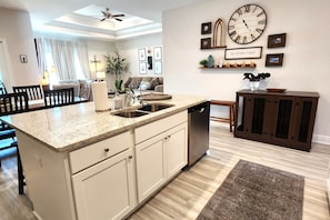 A modern kitchen with a granite countertop, stainless steel dishwasher, and a large wall clock.