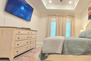Une chambre à coucher avec un lit, une commode, un téléviseur fixé au mur et une fenêtre avec des rideaux.