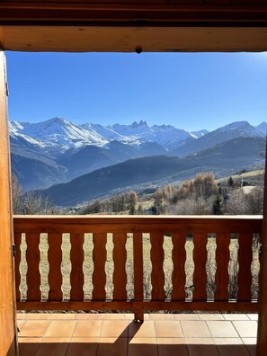 Ein Balkon mit Holzgeländer mit Blick auf eine gebirgige Landschaft, deren Gipfel mit Schnee bedeckt sind.