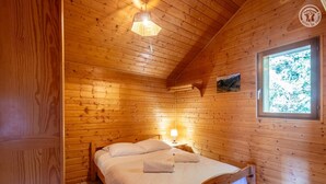 A wooden cabin room with a bed, a window, and a wall-mounted light fixture. - LA COCHETTE - JARRIER (JARRIER)