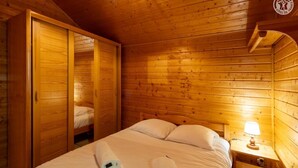A wooden room with a bed, two nightstands, a lamp, and a wardrobe. - LA COCHETTE - JARRIER (JARRIER)