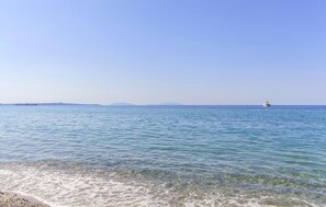 A calm sea with a clear sky, a distant shoreline, and a small boat.
