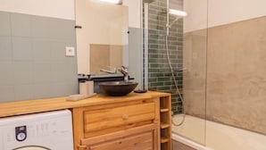 Un baño pequeño con lavadora, tocador de madera y mampara de vidrio.