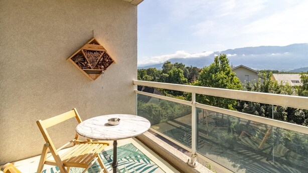 Un balcón con mesa y sillas, un estante de madera con leña, y una vista despejada de un paisaje montañoso.