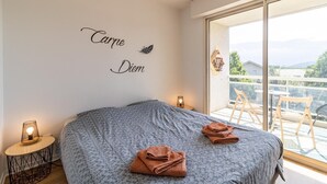 Un dormitorio con una cama grande, una mesita de noche con lámpara y un ventanal con vistas al exterior.