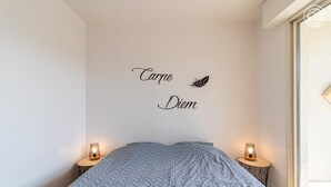 Un dormitorio con cama, dos lámparas de noche, una pared con una frase decorativa y una ventana.