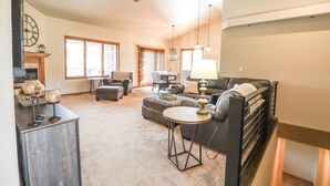 A living room with a ceiling fan, a fireplace, and a large window with curtains. - Serene Golf Course Home Getaway with Hot Tub (Sturgis)