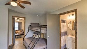 Ein kleines Zimmer mit Etagenbett, Deckenventilator, kleinem Badezimmer mit Spiegel und einer Tür zu einem Wohnbereich mit Sofa und Couchtisch.