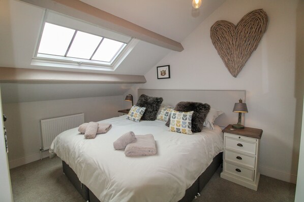 A bedroom with a skylight, a heart-shaped wall decoration, a bed with multiple pillows, and a bedside table with a lamp. - Cosy Cottage, Ambleside - a cottage that sleeps 4 guests in 2 bedrooms (Ambleside)