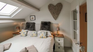 Une chambre dotée d’une lucarne, d’une décoration murale en forme de cœur, d’un lit agrémenté d’oreillers à motifs, de deux lampes de chevet et d’une table de chevet avec des tiroirs.