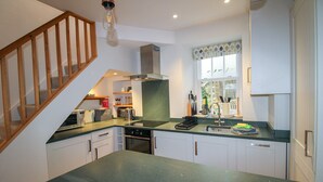 Une cuisine moderne avec un plan de travail vert, des armoires blanches, un four encastré et un escalier en bois.