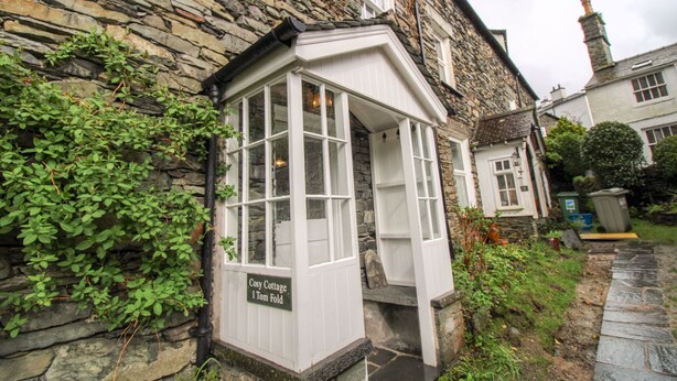 Une petite maison en pierre avec un petit porche et une enseigne indiquant : « Cosy Cottage 1 Tom Fold ».