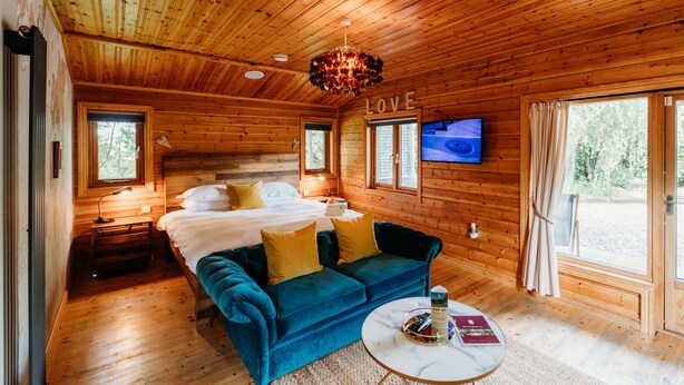 A cozy cabin room with a bed, blue sofa, and a TV on the wall.