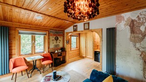 A cozy cabin interior with wooden walls, a dining area with a table and chairs, a blue sofa, and a map on the wall.