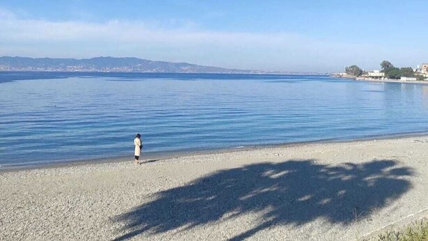 A beach with calm water, a person walking, and distant hills. - 76 Avenue Suite - Very close to the city center (Reggio Calabria)