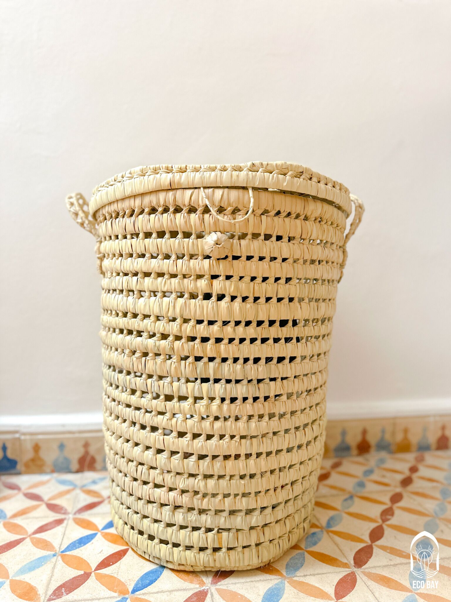 A woven basket with handles, placed on a patterned tile floor.