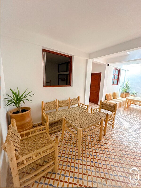 A room with a patterned floor, wicker furniture, a potted plant, and a view through an open door. - Eco Bay hostel  (Aourir)