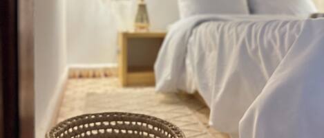 A room with a bed, a woven basket, a nightstand, and a wall-mounted light fixture.