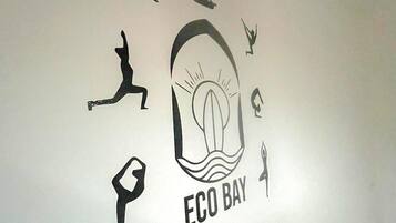 A wall with various black silhouettes, including a person in a hat, a person in a yoga pose, and a person jumping. The central image is a stylized eye with the text "ECO BAY" below it.