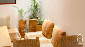 A cozy room with a wooden table, woven chair, and a sofa with cushions. There are three hanging light fixtures with twisted ropes. - Eco Bay hostel  (Aourir)