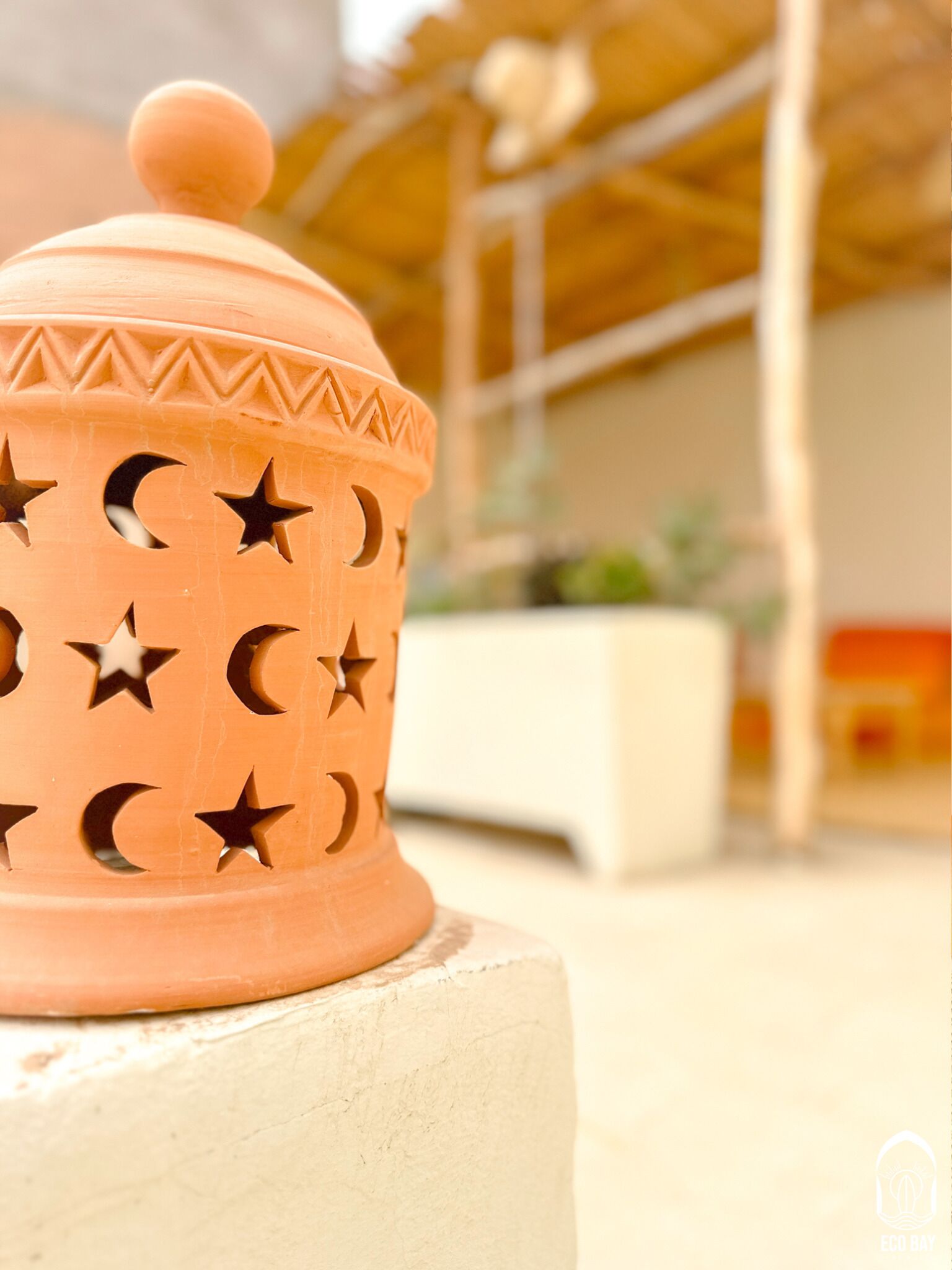 A terracotta pot with star and crescent cutouts, placed on a white pedestal.