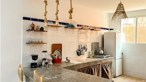 A kitchen with a marble countertop, wooden chairs, and a hanging light fixture. - Eco Bay hostel  (Aourir)