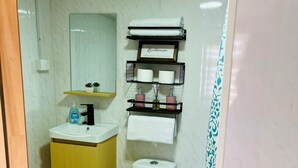 Un baño pequeño con inodoro, lavamanos y un estante sobre el inodoro con artículos de aseo.