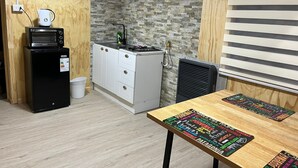 Cocina compacta con microondas, estufa y armarios blancos. Hay un bote de basura pequeño y una mesa con un mantel individual colorido.