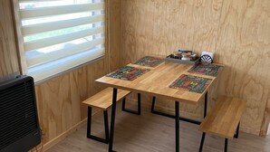 Una habitación pequeña y acogedora con una mesa de madera y bancos, un radiador y una ventana con persianas.