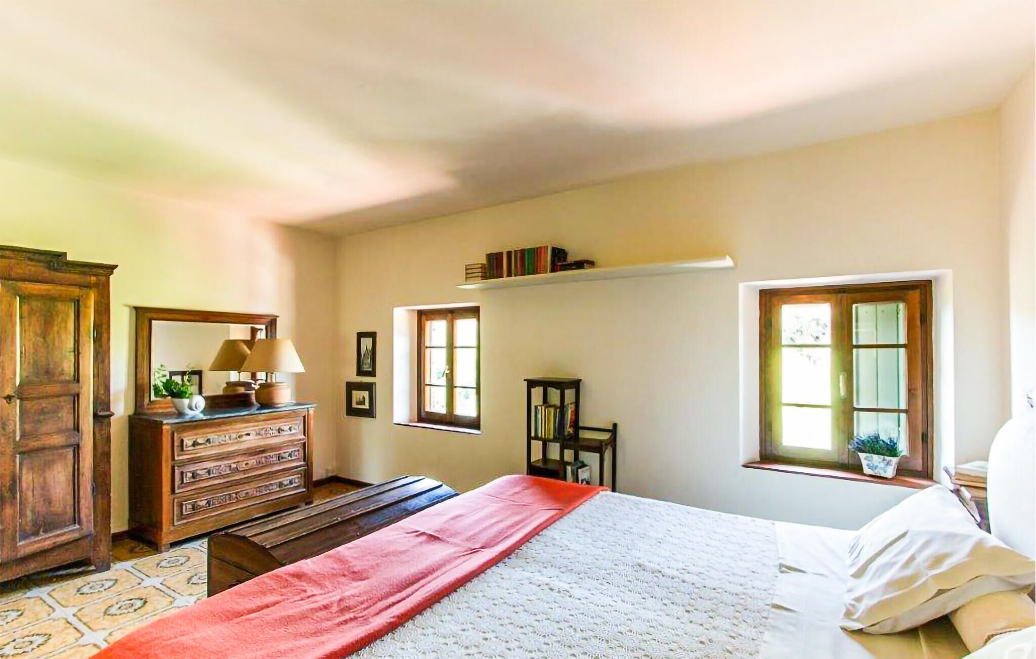 A bedroom with a bed, dresser, and two windows.