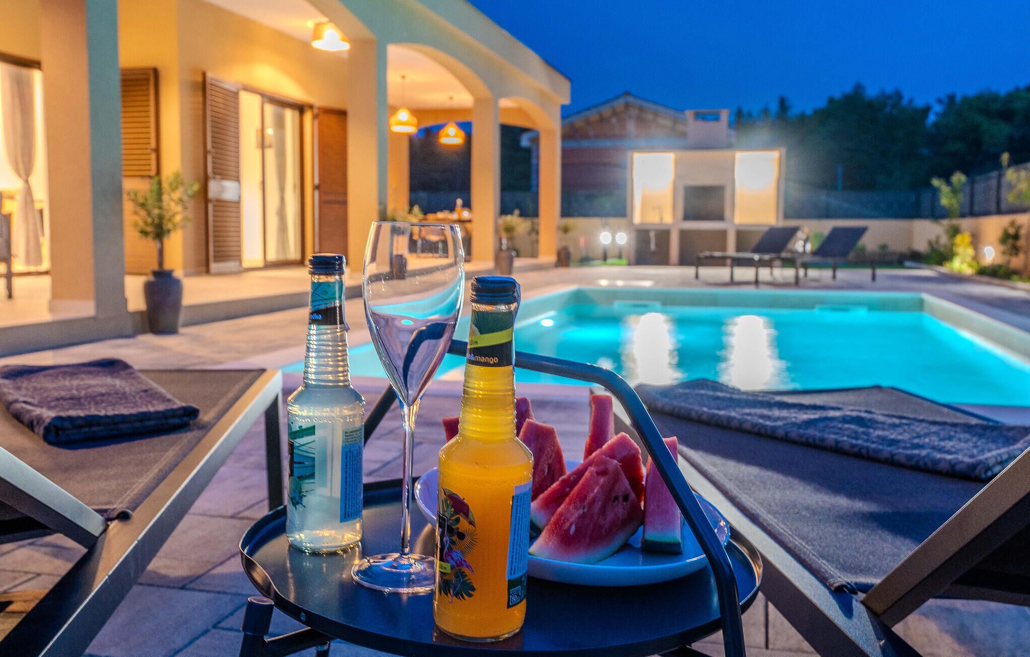 A poolside setting with lounge chairs, a table with drinks, and a pool in the background.