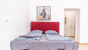 Una cama con cabecera roja, ropa de cama gris y una obra de arte enmarcada encima.