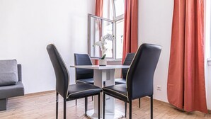 Un comedor con una mesa y cuatro sillas, una ventana con cortinas rojas y un sofá gris.