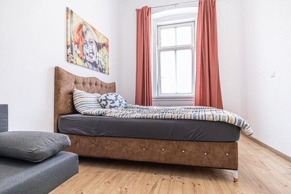 Ein Schlafzimmer mit einem Bett, einem Sofa, einem Fenster mit Vorhängen und einem Gemälde an der Wand.