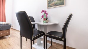 A room with a white table, two black chairs with gold trim, a small vase with flowers, and a framed picture on the wall. - Cozy Central Room, Only 15-Min Walk to Prater (Vienna)