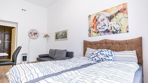 A bedroom with a large bed, a headboard, a painting, a clock, and a chair. - Cozy Central Room, Only 15-Min Walk to Prater (Vienna)