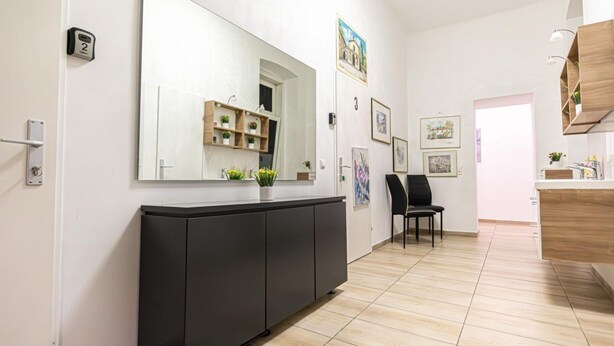 A modern interior with a large mirror, a black cabinet, a wooden shelf with plants, and a chair. - Lovely Room @2nd Vienna, Only 10-Min to Augarten (Vienna)