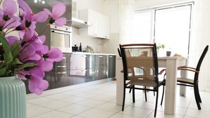 A modern kitchen with stainless steel appliances, a dining area with wicker chairs, and a large window providing natural light.