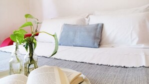 A neatly arranged bedroom with a bed, pillows, a blanket, and a small table with a book and two glass bottles containing plants.