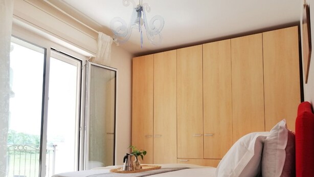 A bedroom with a bed, a wooden wardrobe, a chandelier, and a balcony.